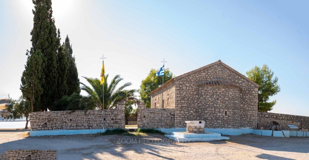 Το πέτρινο εκκλησάκι της Παναγίας Φοινικιάς με κυπαρίσσια και φοίνικα, στις Αλυκές Μεσολογγίου