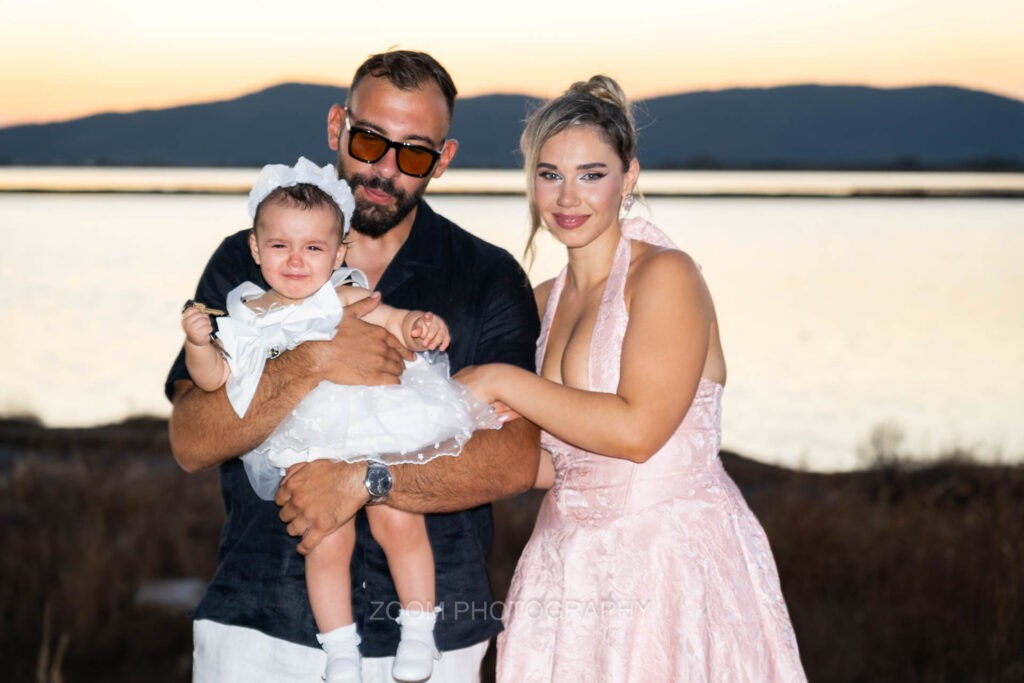 Η μαμά και ο νονός με τη μικρή μπροστά στη λιμνοθάλασσα, στο ηλιοβασίλεμα