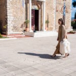 Νονά περπατά στο προαύλιο του ναού κρατώντας τα λευκά βαπτιστικά