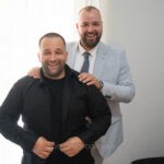 Ο γαμπρός κουμπώνει το πουκάμισό του και ένας φίλος του φτιάχνει τους ώμους