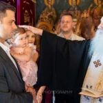 Ο ιερέας ευλογεί τη Μαριάνθη στην αγκαλιά του νονού της στην αρχή της βάπτισης