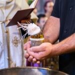 Τα χέρια του νονού κρατούν το λάδι της βάπτισης πάνω από την κολυμβήθρα