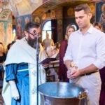 Ο νονός κρατά το μπουκαλάκι με το λάδι δίπλα στην κολυμβήθρα, την ώρα που διαβάζει ο ιερέας