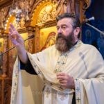 Ο ιερέας σηκώνει ψηλά τον χρυσό σταυρό της Μαριάνθης μπροστά στο ξυλόγλυπτο τέμπλο