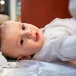 Ο Γεράσιμος με βρεγμένα μαλλιά μετά την κολυμβήθρα, ξαπλωμένος στο λευκό σεντόνι