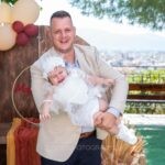 Ο Παναγιώτης κρατά τη Μαριάνθη μπροστά στον στολισμό, με το Αγρίνιο στο βάθος
