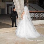 Η νύφη με το μακρύ πέπλο στο προαύλιο και ο γαμπρός στο βάθος